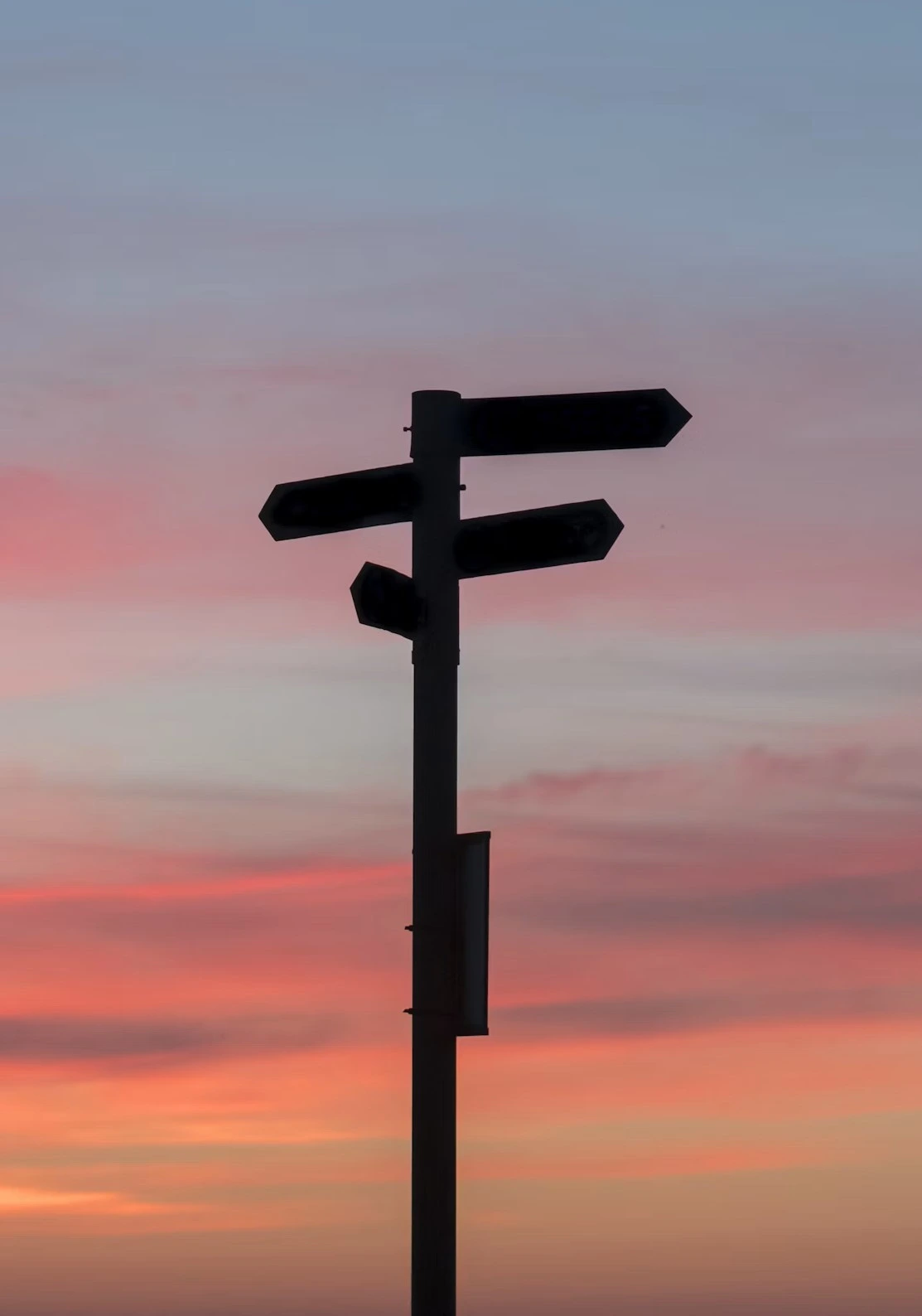 A silhouette of a post with multiple signs pointing in different directions