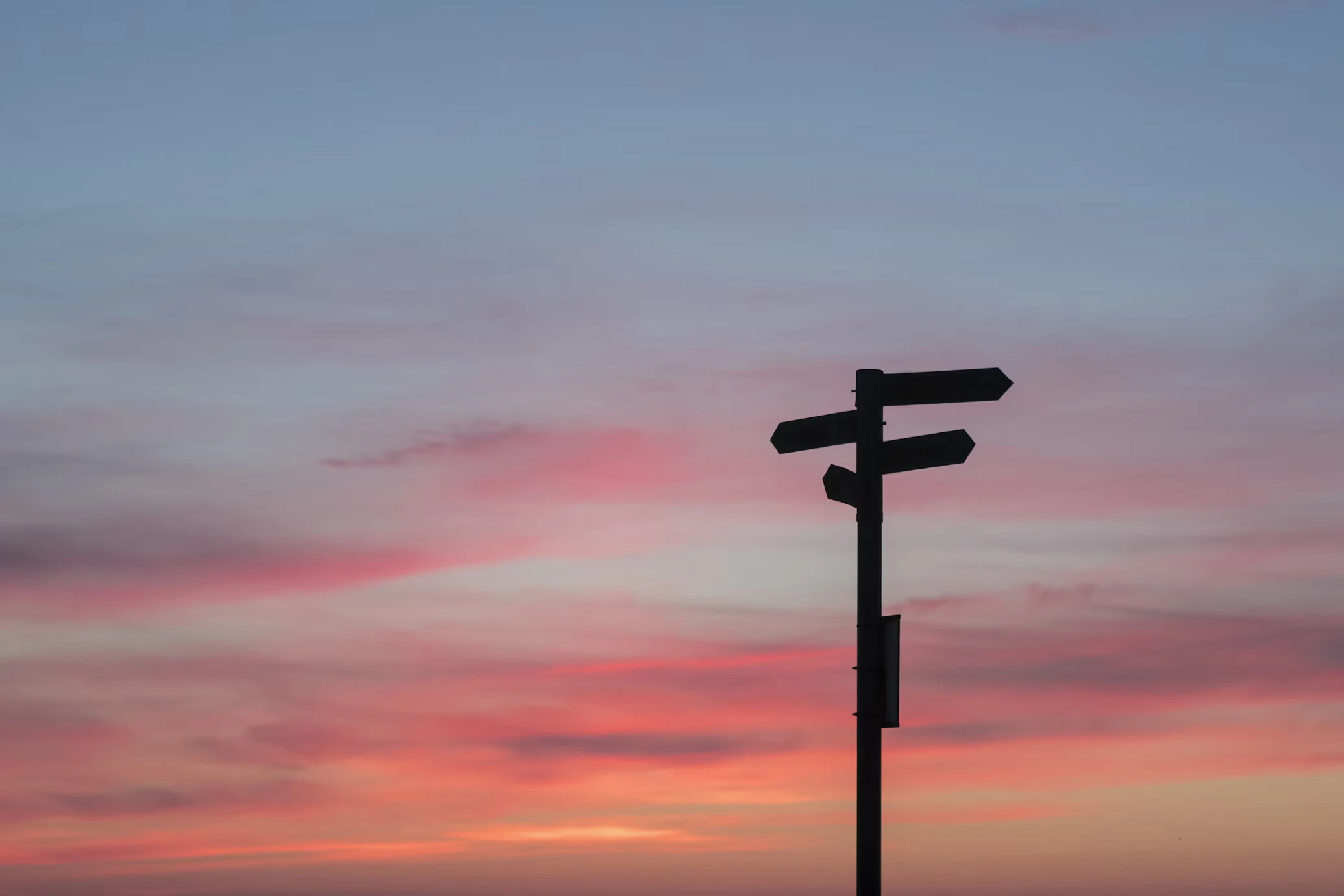 A silhouette of a post with multiple signs pointing in different directions